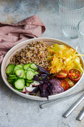 High angle of bowl with delicious buckwheat containing sliced fresh basil plant with cabbage and cucumber with cutlery and glasses placed on gray table with napkin - ADSF46238