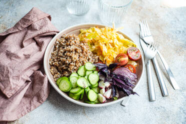 High angle of bowl with delicious buckwheat containing sliced fresh basil plant with cabbage and cucumber with cutlery and glasses placed on gray table with napkin - ADSF46239