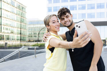 A happy couple captures a moment together, taking a selfie with a cityscape in the background - ADSF46264