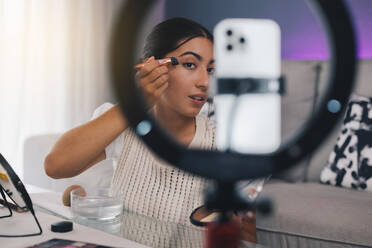 Female video blogger applying make up on face in living room - ADSF46342