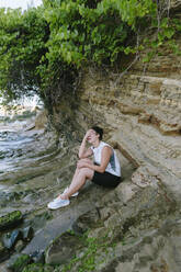 Woman covering face with hand sitting on rock - SIF00763