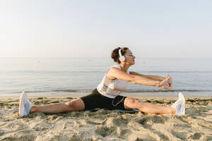 Woman practicing stretching exercise in front of sea at beach - SIF00773