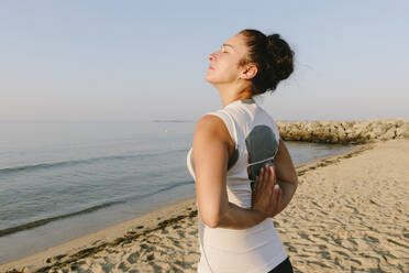 Frau mit hinter dem Rücken verschränkten Händen übt Yoga am Strand - SIF00778