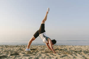 Woman practicing stretching leg exercise at beach - SIF00779
