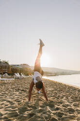 Frau übt am Strand an einem sonnigen Tag Beinstreckübungen - SIF00780