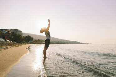 Frau mit verschränkten Händen übt Yoga an einem sonnigen Tag am Strand - SIF00783