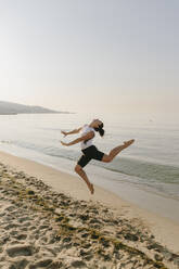 Frau springt am Strand vor das Meer - SIF00785