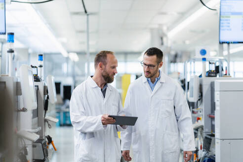 Zwei Mitarbeiter analysieren auf einem Arbeitstreffen in einer Elektronikfabrik Daten auf einem digitalen Tablet - DIGF20163
