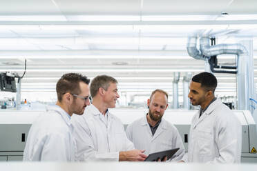 Team of competent electrical technicians in lab coats having meeting in electronics factory - DIGF20189