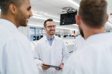 Team of competent electrical technicians in lab coats having meeting in electronics factory - DIGF20191