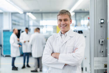 Technician in white lab coat standing in electronics factory with arms crossed - DIGF20224