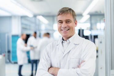 Technician in white lab coat standing in electronics factory with arms crossed - DIGF20225