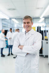 Technician in white lab coat standing in electronics factory with arms crossed - DIGF20226
