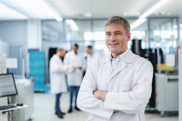 Technician in white lab coat standing in electronics factory with arms crossed - DIGF20227