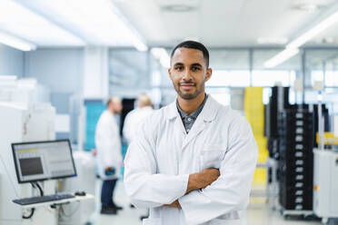 Confident technician smiling with arms crossed while colleagues are talking in electronics factory - DIGF20231