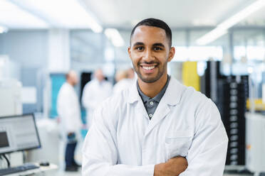 Confident technician smiling with arms crossed while colleagues are talking in electronics factory - DIGF20232