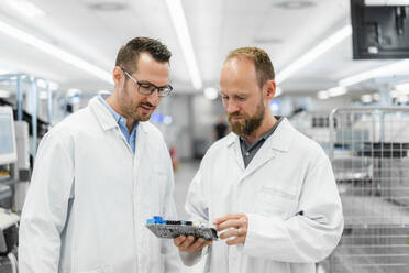 Techniker in weißen Laborkitteln diskutieren über elektronische Bauteile - DIGF20240