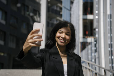 Eine elegante Frau hält einen sonnigen Tag in Georgien mit einem Selfie fest, gekleidet in einen eleganten schwarzen Anzug und mit ihrem Handy - YBF00085