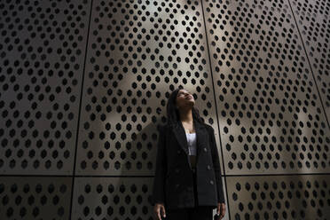 Businesswoman looking up standing near wall - YBF00089