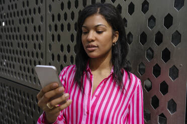 Junge Frau benutzt Mobiltelefon an der Wand - YBF00090