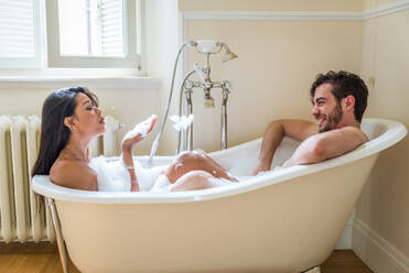 Smiling girl playing in water while taking bath with mother in bathtub at  home stock photo