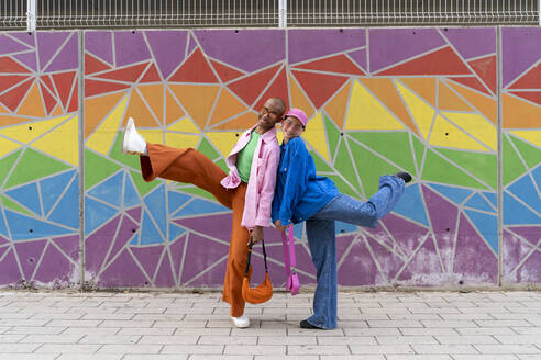 Smiling couple enjoying in front of colorful wall - AFVF09341