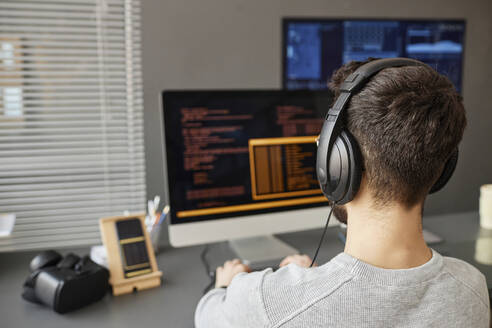 Junger Computerprogrammierer mit Kopfhörern bei der Arbeit an einem Desktop-PC - KPEF00078