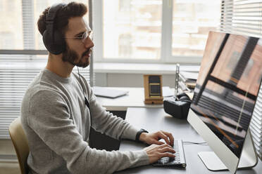 Computerprogrammierer mit Kopfhörern bei der Arbeit an einem Desktop-PC im Büro - KPEF00080