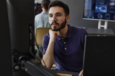 IT-Fachmann mit Hand am Kinn bei der Arbeit am Computer im Büro - KPEF00105