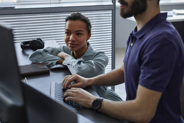 Lächelnder IT-Fachmann mit einem Kollegen, der im Büro an einem Computer arbeitet - KPEF00106