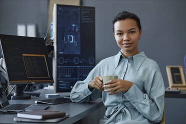 Lächelnder IT-Fachmann sitzt mit einer Kaffeetasse am Schreibtisch - KPEF00124