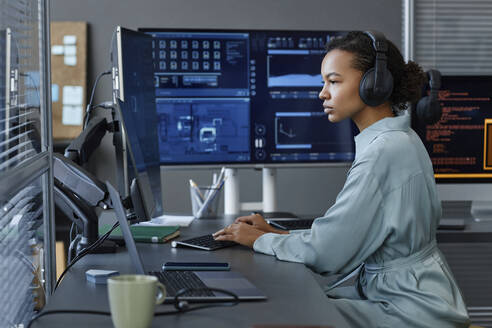 Young computer programmer wearing wireless headphones working on desktop PC - KPEF00131