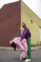 Non-binary person holding woman bending backwards in front of building - AFVF09364