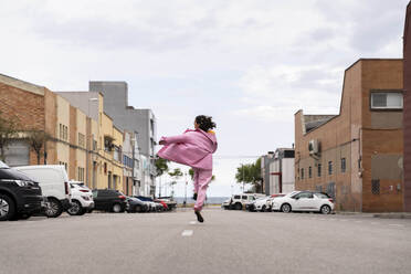 Cheerful woman jumping and walking on road under sky - AFVF09366