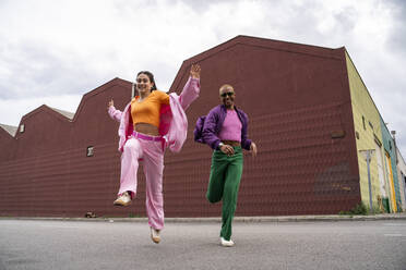 Happy couple running and jumping in front of building - AFVF09388