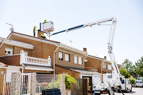 Engineers with colleague holding solar panel on hydraulic platform at roof - JJF01108