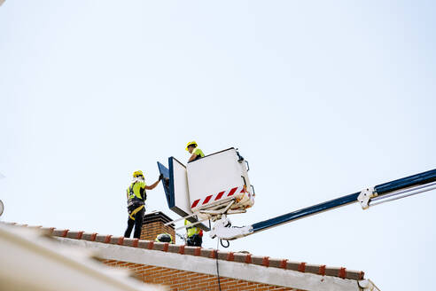 Engineers with colleague holding solar panel on hydraulic platform under sky - JJF01109