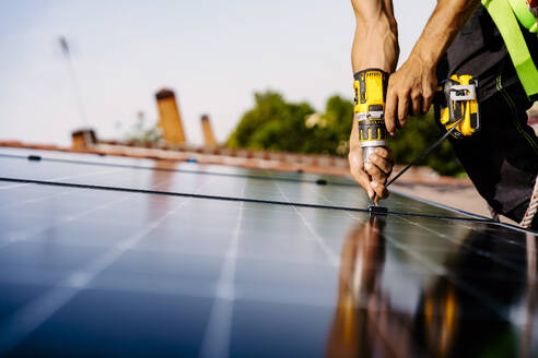 Hände eines Ingenieurs mit Bohrmaschine bei der Installation von Solarmodulen - JJF01134