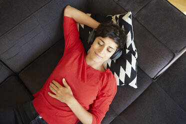 Unwinding in style, this woman indulges in music while lounging on the couch with her headphones on - RBF09286