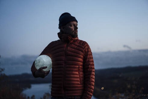 Thoughtful man standing with moon model at dusk - JOSEF20465