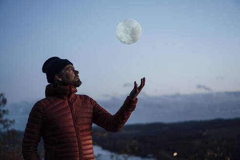 Mature man throwing artificial moon in air under sky - JOSEF20466