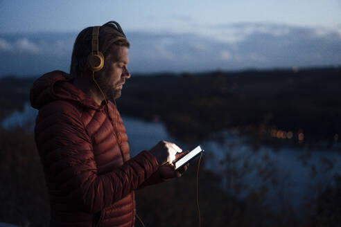 Älterer Mann hört Musik über sein Smartphone in der Nähe eines Sees - JOSEF20480