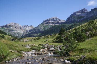 Wasser rauscht über Felsen im Valle de Aisa in den Pyrenäen, Spanien, umgeben von üppigem Grün und Bäumen - ADSF46356