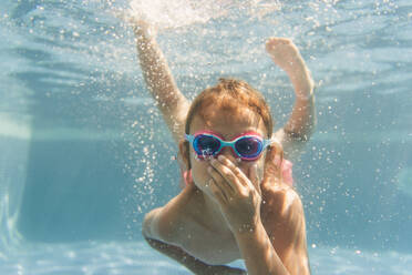 Ein junges Mädchen mit einem strahlenden Lächeln und einer Schwimmbrille genießt ein erfrischendes Bad in einem kristallklaren Pool - ADSF46364