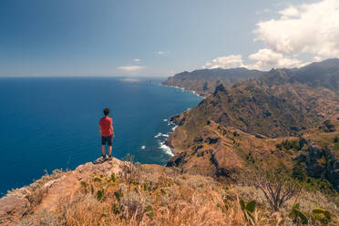 Ein einsamer Wanderer bewundert die atemberaubende Küste Teneriffas vom Rand einer Klippe aus, umgeben von natürlicher Schönheit - ADSF46376