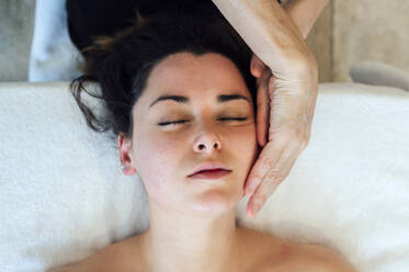 A serene spa experience: A skilled therapist gives a facial massage to a young woman resting on a bed - ADSF46387