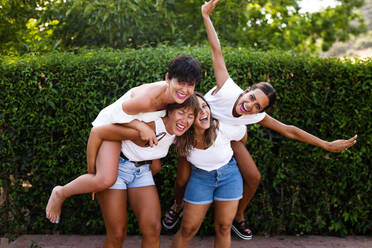 Eine Gruppe glücklicher Frauen, die Spaß haben und gemeinsam lachen, während sie auf der Straße Huckepack nehmen - ADSF46433