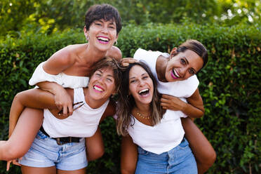 Eine Gruppe glücklicher Frauen, die ein vergnügliches Wochenende verbringen, miteinander lachen und sich auf der Straße Huckepack nehmen lassen - ADSF46435