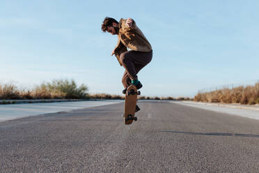 Ein modischer Skater vollführt makellos einen Kickflip, während er auf seinem Skateboard über den glatten Bürgersteig cruist - ADSF46450