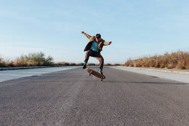 A fashionable skater flawlessly performs a kickflip while cruising on his skateboard on the sleek pavement - ADSF46452